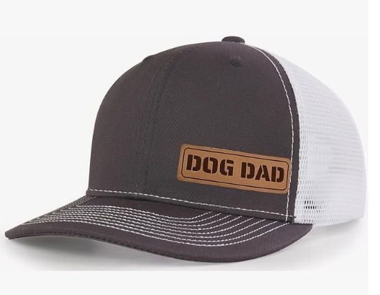 A gray and white baseball cap with a small brown leather tag that says "Dog Dad" on the bottom left of the front.