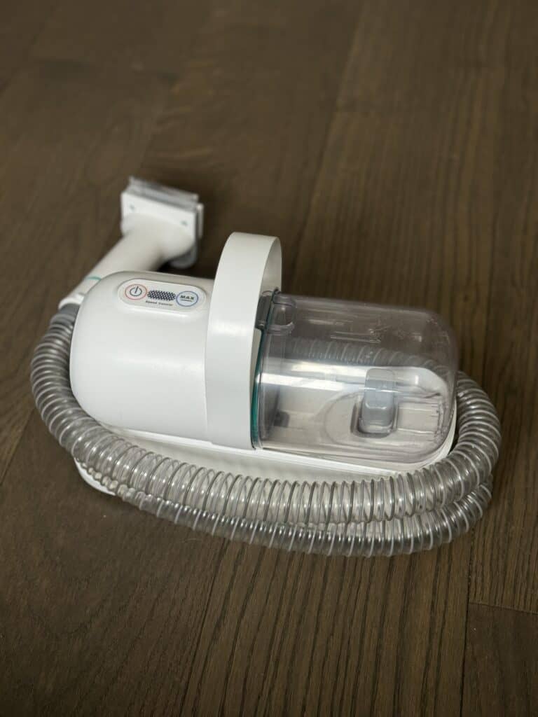 A dog grooming vacuum system laying on a wood floor.