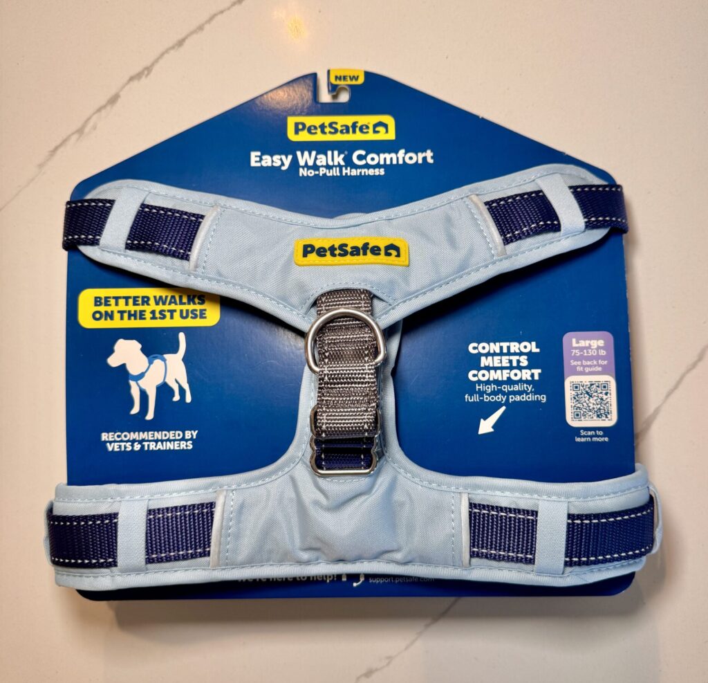 A PetSafe sky blue dog harness with royal blue straps on a blue cardboard display with the title “PetSafe Easy Walk Comfort No-Pull Harness”.