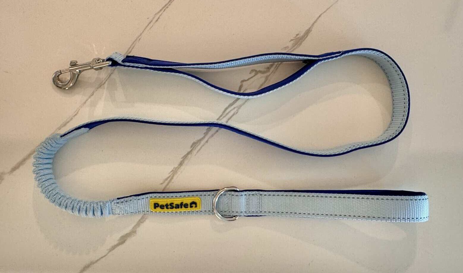 A close-up photograph of a PetSafe dog leash that is sky blue on one side and royal blue on the other, and features a shock-absorbing bungee section and a traffic-control handle towards the clip.